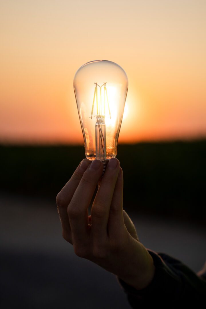 close-up-of-electric-lamp-in-the-hand-on-the-backgoriun-of-a-sunset-renewable-energy-symbol